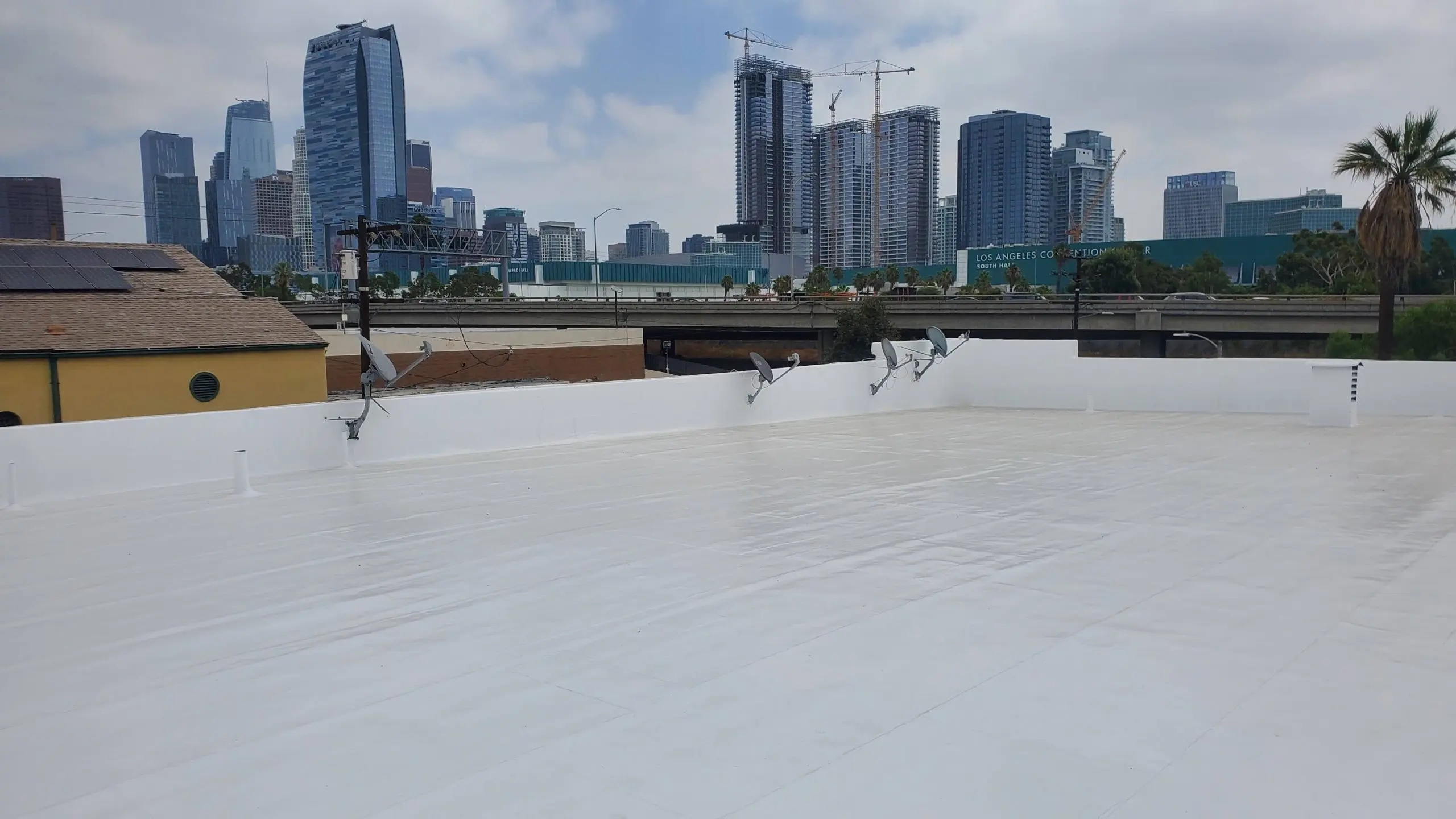 White reflective roof coating on a flat commercial roof with a city skyline in the background