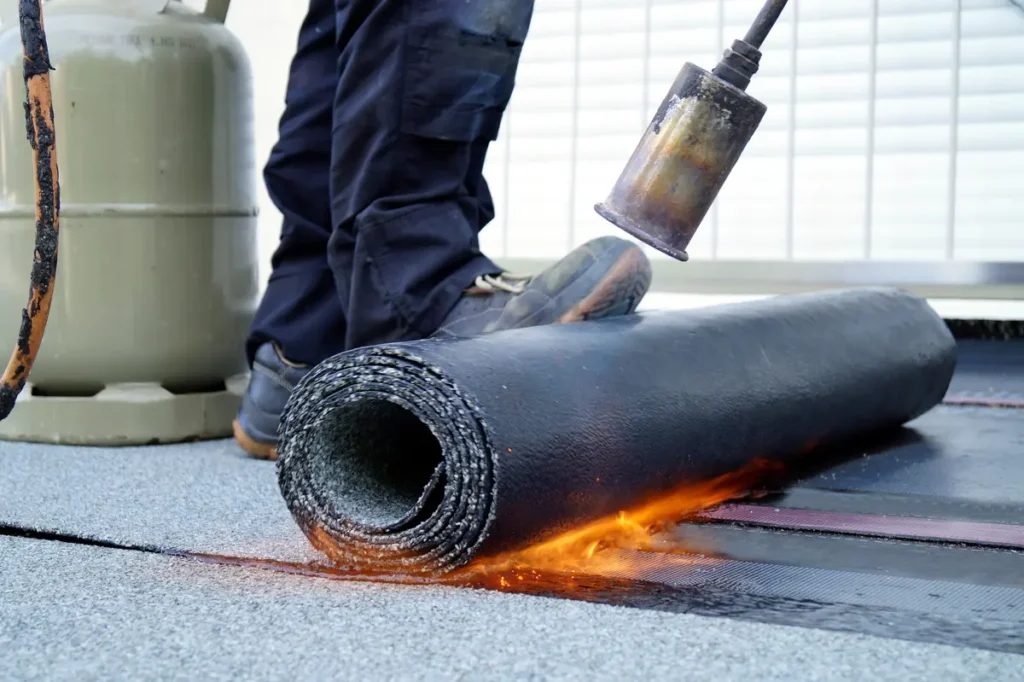 Roofer using a propane torch to seal a rolled roofing membrane during a repair